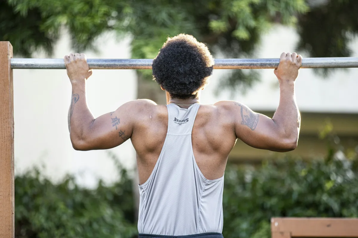 A man seen from behind pulling his chin toward an outdoor pull-up bar