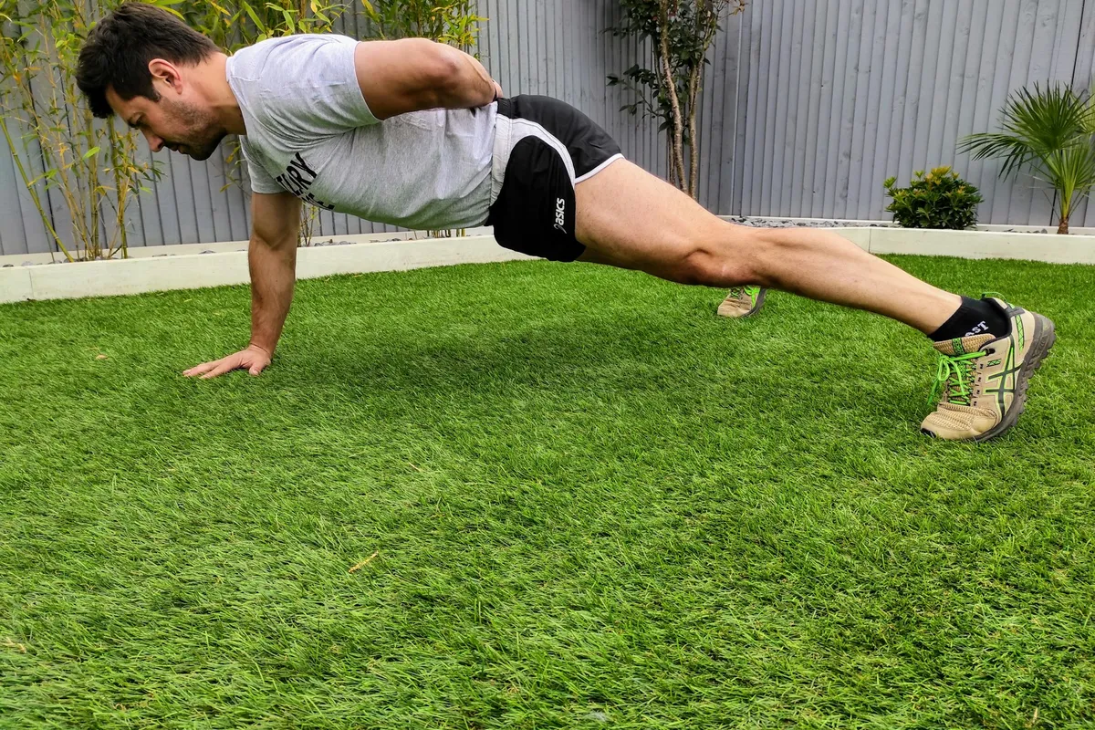 A man doing a push-up on a lawn in a back garden