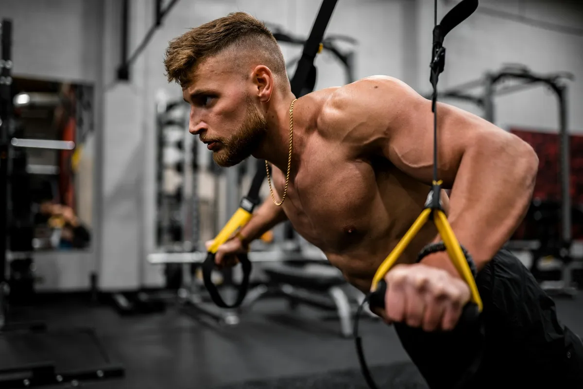A man leaning back and pulling on suspension straps in a gym